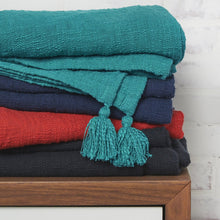 devin throw blankets in teal indigo red and black folded and stacked on a table
