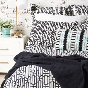 black devin throw blanket styled on geometric bedding against a white brick wall