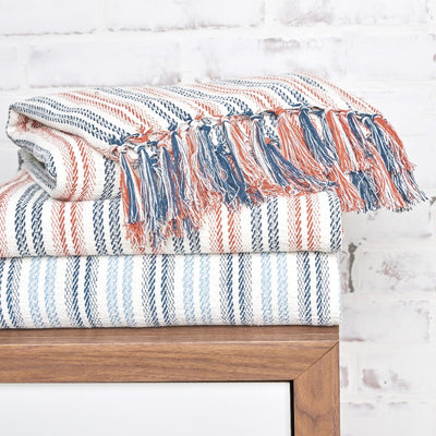 peach blue white striped hugo throw blankets with tassel fringe folded and stacked on a table